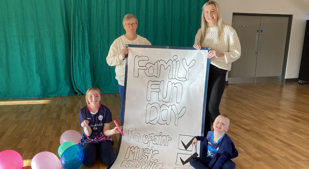 Two female adults holding large Family Fun Day checklist with two children - one with balloons -  ticking off the list